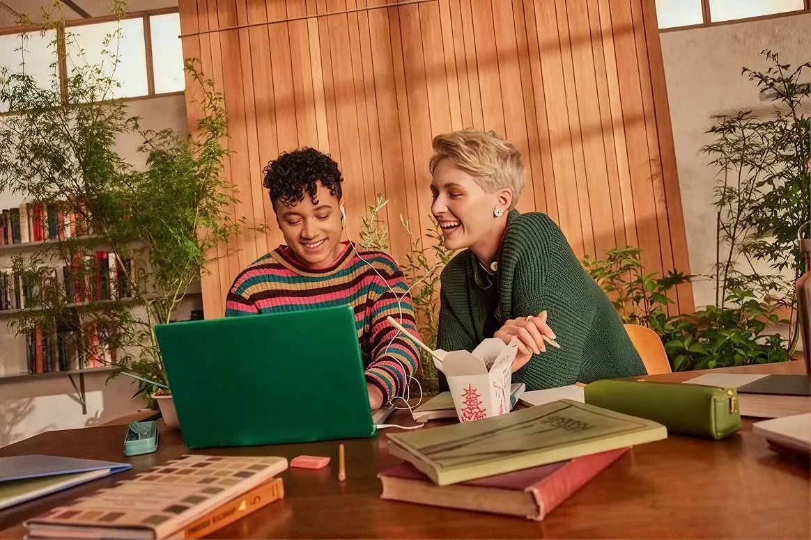 Two international students working through their Spanish university paperwork on a laptop
